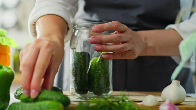 Garlic, active woman Stacks preparing cucumbers in a glass jar for preservation in the housewife's home kitchen. the owner of the farm is at her workplace learning new recipes for canned vegetables