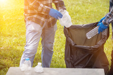 Two man employees use black garbage bags to collect plastic bottles and recyclable waste from the...