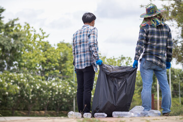 Two man employees use black garbage bags to collect plastic bottles and recyclable waste from the lawn and sidewalks for recycling. Concept of sorting plastic waste for recycling