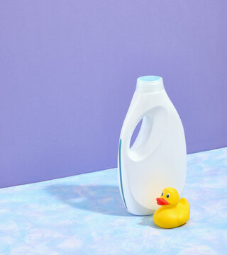 A white big bottle of laundry detergent and shadow. Yellow little rubber duck on the table. Space for text.