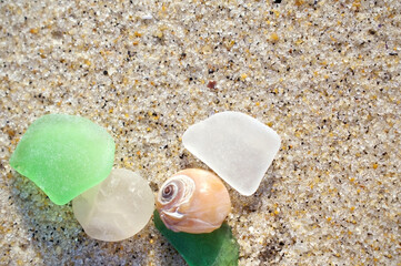 summer close up flatlay of seaglass and a shell on beach sand