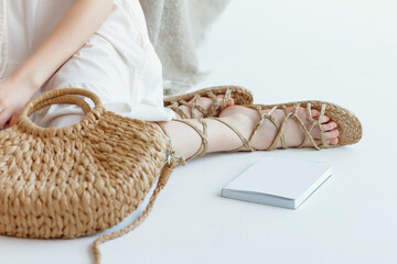 Summer eco style. A girl in a white dress sits on the floor with a bag on her lap, wrapped in...