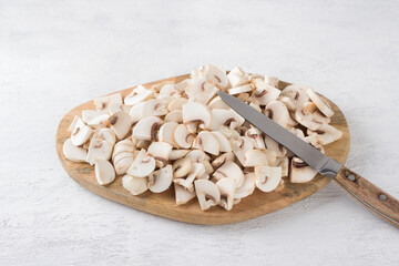 Wooden board with sliced champignon mushrooms on a light gray background, cooking vegan food