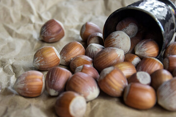 Inshell hazelnuts spilled out of an overturned metal bowl on the background of crumpled craft paper. Close-up. Copy space. Shallow depth of field. Selective focus.