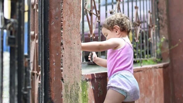 Beautiful Latina baby standing outside her house next to the gate, smiling and playing.