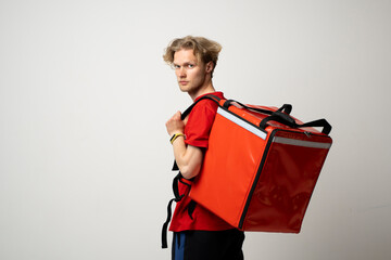 Young courier in a red uniform with thermo bag on white background. Food delivery service.