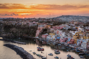Beautiful sunset at Procida island. Sun setting behind the colorful houses of Corricella port, Campania region, Italy