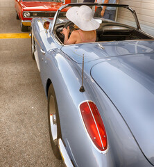 Woman in white summer hat drives sports car at vintage automobile exhibition. 
