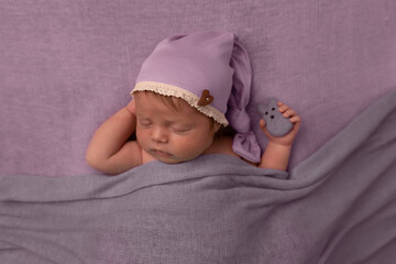 portrait of sweet beautiful newborn baby girl under blanket covers in bed sleeping in natural window light wearing sleepy cap holding felted rabbit for spring easter holiday