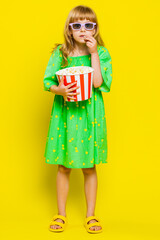 Excited young cute school girl in 3D glasses eating popcorn, watching interesting tv serial, sport game, film, online social media movie content. Teen female child kid on yellow background. Vertical