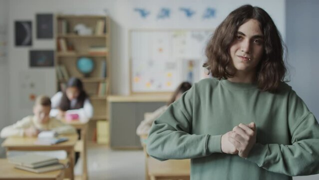 Selective focus medium length portrait of cheeky teenage boy with long hair holding toothpick getting ready to bully someone