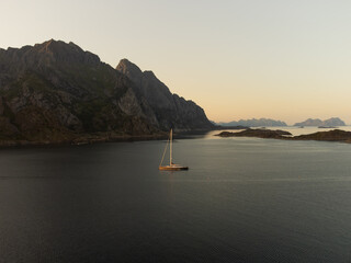 Sailboat in Lofoten, under the midnight sun. Mountains in the horizon, clear skies, near...