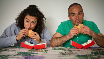 Young couple sits at a table and eats a burger with a fun attitude simulating piggishness