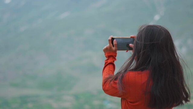 Tourist girl shooting video, photos with mobile phone in mountains. Carefree female blogger shooting travel vlog in Lahaul, India. Solo tourist using cellphone for photography
