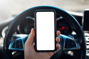 Close-up male hand holding smartphone with blank on screen against background of steering wheel of car.
