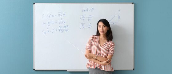 Asian math teacher near flipboard in classroom