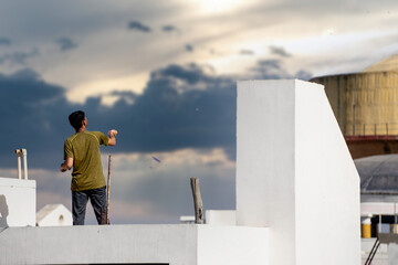 Slow motion shot of man on roof of white building flying kite with multiple kites visible in...
