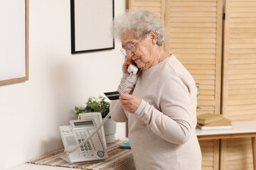 Senior woman with credit card talking by telephone at home - obrazy, fototapety, plakaty