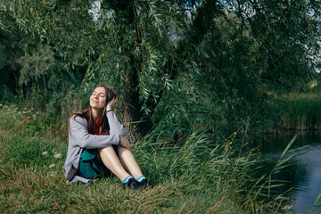 Obraz premium young woman sits on the bank of the river and thinks.Mysterious girl thinks and dreams.positive photo.beautiful self-confident woman. joyful and inspired.feels freedom.Loneliness,thoughts and dreams.
