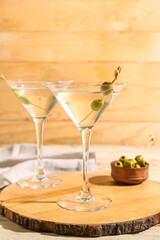 Glasses of tasty martini and olives on light wooden table