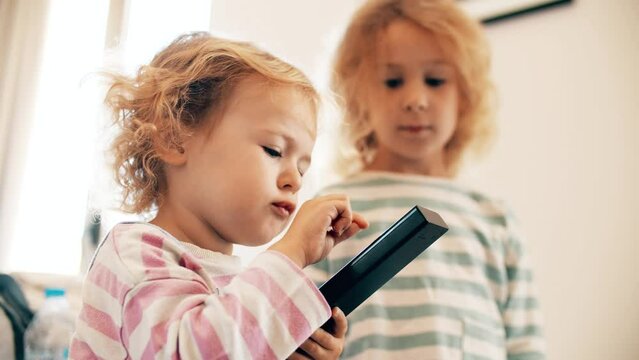 Two adorable little sisters watch TV together and use a TV remote to switch channels