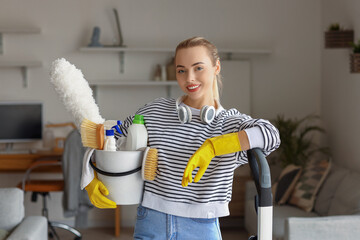 Young woman with bucket of cleaning supplies at home