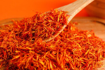 Fototapeta premium Wooden board and spoon with pile of saffron on orange background