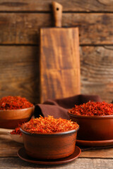 Bowls with pile of saffron on wooden background