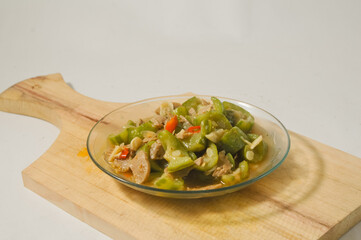 Sauteed gambas or luffa gourd with sliced meatballs served on a small plate on a wooden board isolated on a white background.