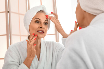 Mature woman applying facial cream near mirror in bathroom, closeup