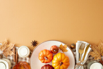 Fall decor inspiration idea. Top view of plate, cutlery, tablecloth, pumpkins, glass, candles, dry leaves, napkin, anise, cinnamon, acorns on pastel brown background with empty space for ad or text