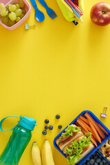 Healthy snack during the educational process. Top view vertical shot of lunchbox, sandwiches and fresh snacks, bottle, case with pens on yellow background with empty space for promo or text