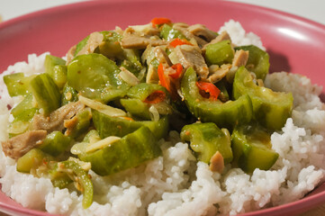 A plate of white rice with stir fried gambas or luffa gourd and sliced meatballs on a wooden cutting board isolated on a white background.