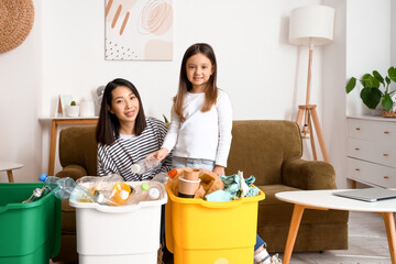 Asian mother with her little daughter sorting garbage in recycle bins at home