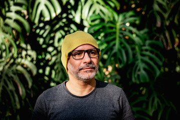 Portrait of mature man with yellow beanie in front of tropical leaves