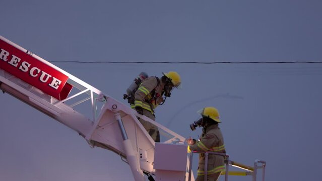 Firefighter climbing down firetruck ladder in full equipment and breathing mask, hero, hazardous, emergency services, fire, smoke. 4K 24FPS.