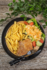 Fried pork chop in breadcrumbs, served with fries and salad.