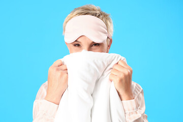 Mature woman with sleeping mask and blanket on blue background, closeup
