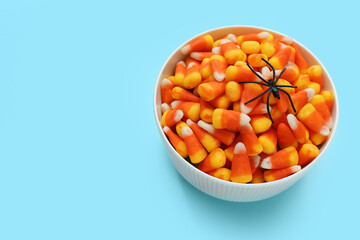 Bowl with tasty Halloween candy corns and spider on blue background, closeup