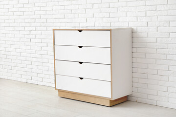 Stylish white chest of drawers near light brick wall in room