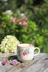 A beautiful ceramic coffee cup  with flowers on the wooden table in the garden. Selective focus. 