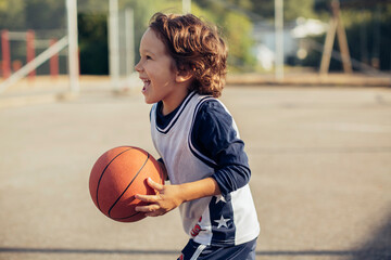 Naklejka premium Young boy playing basketball on a basketball court outside in the suburbs