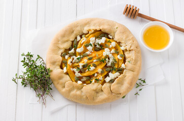 Homemade galette with pumpkin, feta cheese, honey, pumpkin seeds and thyme on white background, top view