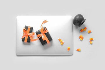 Composition with modern laptop, gift boxes and tasty candy corns for Halloween on white background