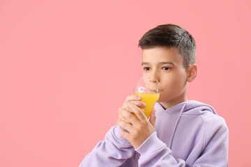 Little boy drinking orange juice on pink background