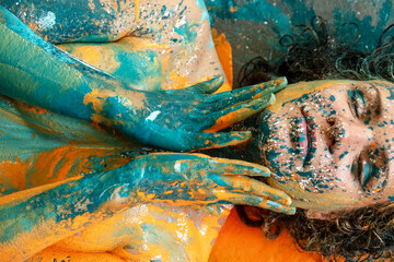 portrait and torso of a sexy young nude woman arms covering breasts in turquoise green and orange color painted decorative. Creative expressive abstract body painting art