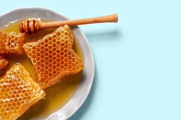 Plate with sweet honeycombs and dipper on blue background