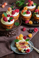 Cupcakes with butter cream and raspberry curd, decorated with berries on a wooden surface.