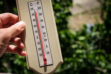 Ice cubes melting in direct sun next to a home thermometer showing over 40 degrees Celsius during a heat wave - 630489543