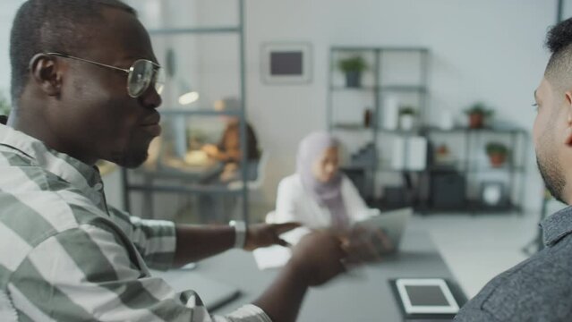 Selective focus shot of African American and Middle Eastern men standing in office defaming their female colleague